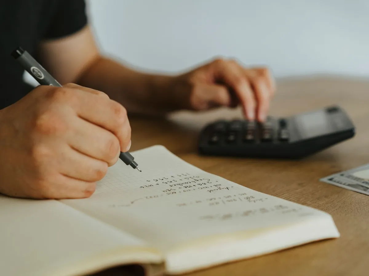 Main calculant un budget au stylo à côté d'une calculatrice sur un bureau en bois, avant de lancer une campagne de retargeting TPE locale
